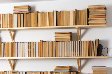 Light wooden bookshelves with hardback overturned books in white interior, home library