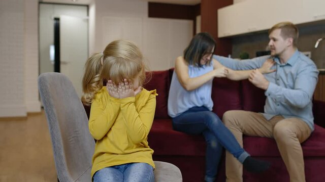 Caucasian child girl kid is suffering and crying from quarrels between parents in family at home. Angry man and woman quarrelling and fighting in living room. Scandal, conflict, crisis. Psychology