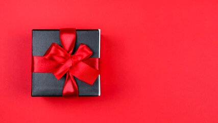 gift box on red background.

Black gift box with ribbon on the left on a red background with space for text on the right, top view close-up.