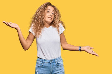 Beautiful caucasian teenager girl wearing casual white tshirt clueless and confused expression with arms and hands raised. doubt concept.