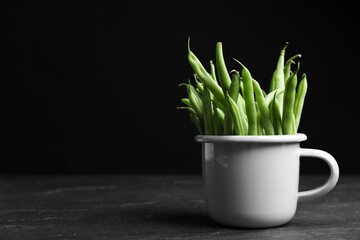 Fresh green beans in white mug on black table, space for text