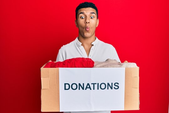 Young arab man holding donation box with clothes making fish face with mouth and squinting eyes, crazy and comical.