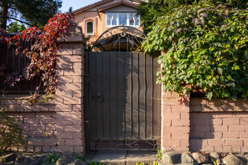 Fototapeta premium A brown metal gate in a pink brick fence. Entrance from the street