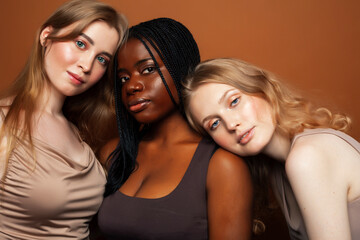 Obraz premium young pretty caucasian, afro, scandinavian woman posing cheerful together on brown background, lifestyle diverse nationality people concept
