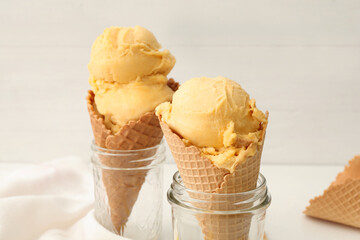 Delicious yellow ice cream in wafer cones and glass jars on table, closeup