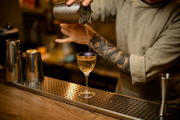 man bartender carefully pouring drink from measuring cup into glass at the bar