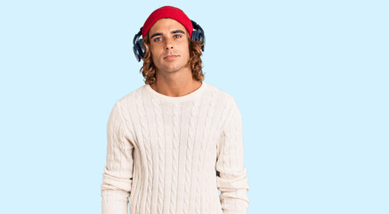 Young hispanic man listening to music using headphones relaxed with serious expression on face. simple and natural looking at the camera.