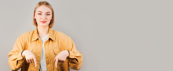 Clothing design and advertisement content. Smiling young woman looking at camera, pointing fingers down © Яна Солодкая