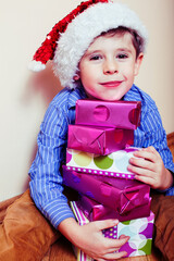 little cute boy with Christmas gifts at home wearing red Santas hat. closeup emotional happy smiling in mess with toys, lifestyle holiday people concept