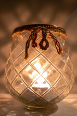 Glass candle holder with burning tea candle with reflection on a surface