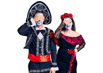Young couple wearing mexican day of the dead costume over background smiling and laughing with hand on face covering eyes for surprise. blind concept.