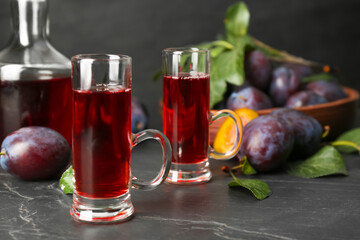 Delicious plum liquor and ripe fruits on black table. Homemade strong alcoholic beverage
