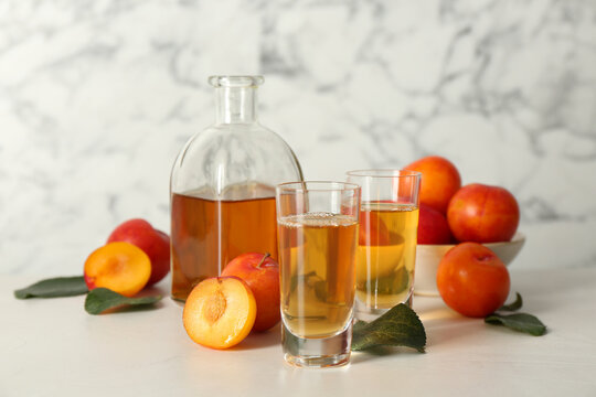 Delicious plum liquor and ripe fruits on white table. Homemade strong alcoholic beverage