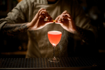 bartender holds lemon peel and skillfully sprinkles on glass with bright cocktail.