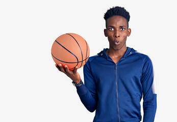 Young african american man holding basketball ball scared and amazed with open mouth for surprise, disbelief face