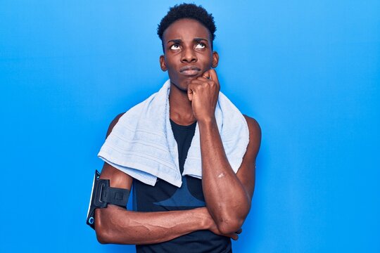 Young african american man wearing sportswear and towel thinking concentrated about doubt with finger on chin and looking up wondering