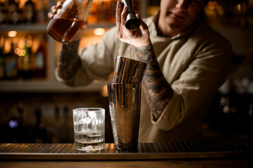 barman gently pours drink from metal jigger into shaker on bar counter