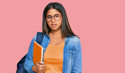 Young latin girl wearing student backpack and holding books looking sleepy and tired, exhausted for fatigue and hangover, lazy eyes in the morning.