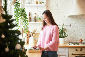 A woman makes Christmas decor in a light loft room, she smiles
