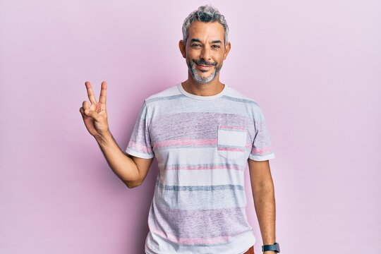 Middle age grey-haired man wearing casual clothes smiling with happy face winking at the camera doing victory sign. number two.