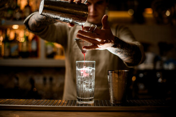bartender holds sieve over transparent glass and gently pours cocktail from shaker.