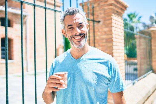 Middle age grey-haired man drinking take away coffee walking at street of city.