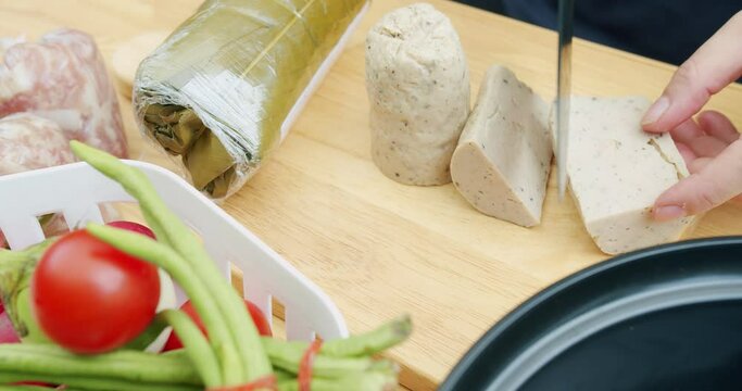 top view hands using kitchen knife cutting Vietnamese Pork Sausage on wooden board, preparing cooking yummy spicy pork sausage salad