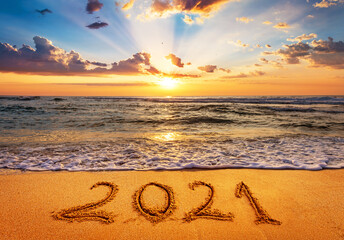 Happy New Year 2021 is coming concept. Number 2021 written on seashore sand at sunrise.