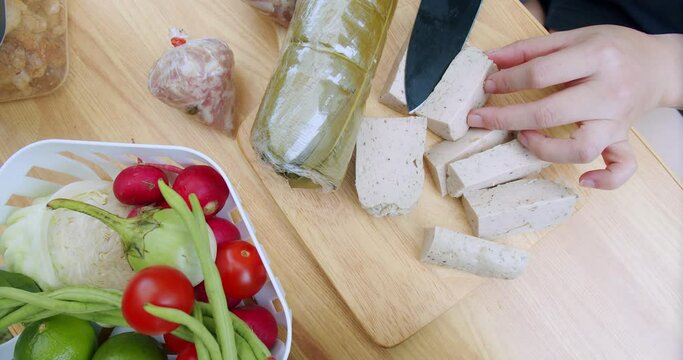 top view hands using kitchen knife cutting Vietnamese Pork Sausage on wooden board, preparing cooking yummy spicy pork sausage salad