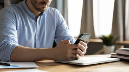Close up cropped view businessman sit at office desk holding smartphone typing respond texting answer to client, solving issues distantly using modern wireless device and internet connection concept