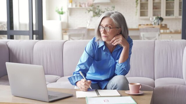 Middle aged older woman watching business training, online webinar on laptop computer remote working or social distance learning from home. 60s businesswoman video conference calling in virtual chat.