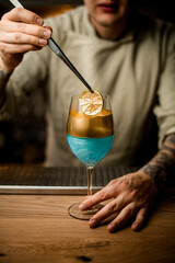 bartender holds slice of citrus over wine glass decorated with gold