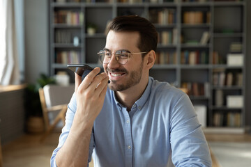 Businessman sit in office holds smartphone leave voice message, solve business issues remotely, use...