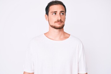 Young handsome man wearing casual white tshirt smiling looking to the side and staring away thinking.