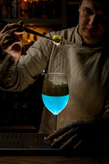 bartender accurate holds golden piece of ice over steaming wine glass and look at it