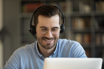 Man wear glasses wireless headset looks at pc screen smiles talk to friends distantly by video...