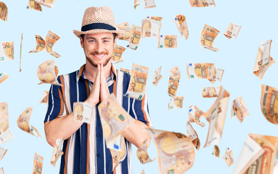 Young handsome caucasian man wearing summer hat praying with hands together asking for forgiveness smiling confident.