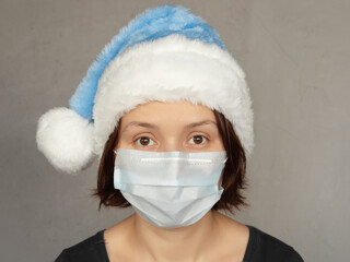 young woman in medical mask and Santa Claus hat on gray concrete background