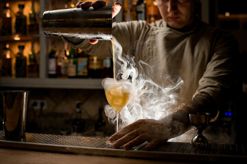 view of man pouring steaming drink from shaker cup into wine glass