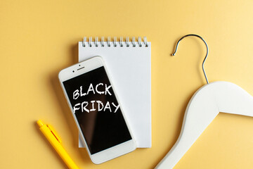 Black friday sales concept. Empty hanger, notepad and phone with Black Friday inscription on yellow background