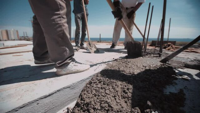 Workers level cement with a shovels on a construction site