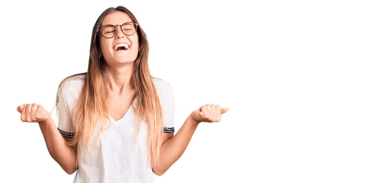 Beautiful caucasian woman wearing casual clothes and glasses pointing thumb up to the side smiling happy with open mouth