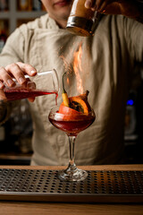 man bartender add ingredients to glass with pumpkin and pepper inside and makes fire over it