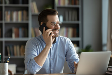 Smiling good-looking businessman in glasses sit at workplace desk in modern office room using...