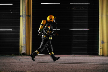 Brave fireman in protective uniform with full equipment running to taking care of fire.