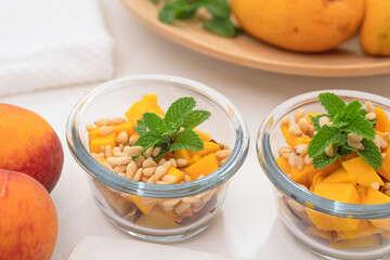 Fruit salad in a glass bowls. Mango, peaches, pine nuts and mint leaf close up.