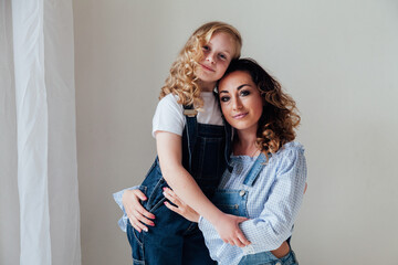 Mom brunette and daughter blonde in jeans sit on the floor