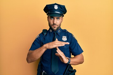 Handsome hispanic man wearing police uniform doing time out gesture with hands, frustrated and...