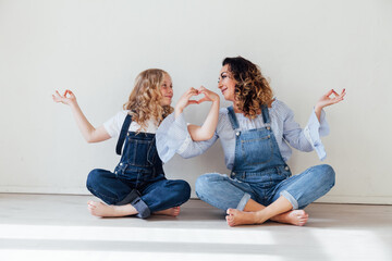 Mom and daughter in jeans are holding hands sitting on the floor