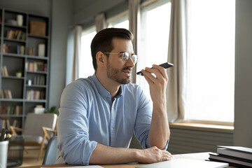 Man sit at desk at home office room holding smart phone communication device using loudspeaker...